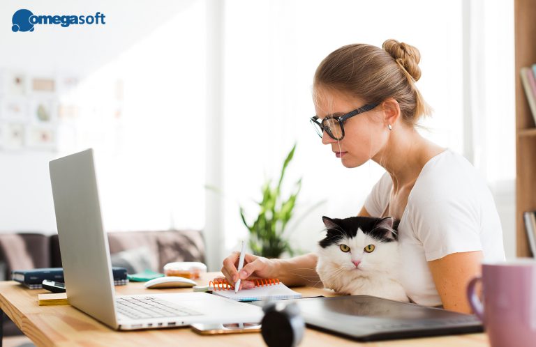 Kobieta z kotem na kolanach, otwartym laptopem i pisząca coś w notatniku